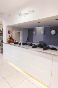reception of a hotel with clocks on the wall, white reception desk and the word reception on the wall above
